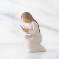Side view of kneeling female figure in cream dress, with wire butterfly on extended hands, on marble background