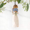 Figure in cream dress, holding large bouquet of blue forget-me-not flowers up to face. Hook and loop affixed to figure's head