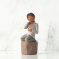 Front view: Figure of darker-skin child, kneeling on rock, holding wire circle with ‘love you’ written in wire