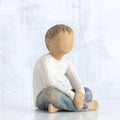 Small little boy figurine sitting down faceless, wearing white shirt and blue jeans
