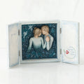 Open light wooden book with three parts - center is blue sky with two carved in faceless boy and girls hugging one another