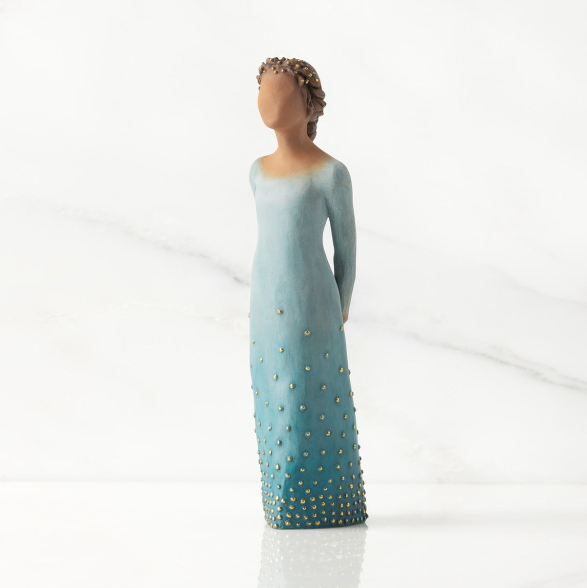 Front/left view: Darker-skin figure, arms clasped behind back, hair and deep blue ombré garment dotted with gold leaf