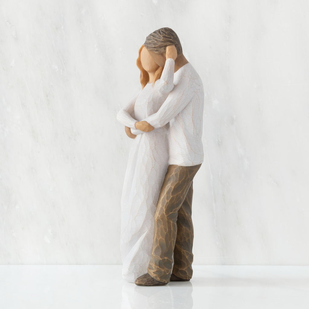 Left view of couple, standing with arms around each other. Woman has lighter skin and hair; man has darker skin and hair.