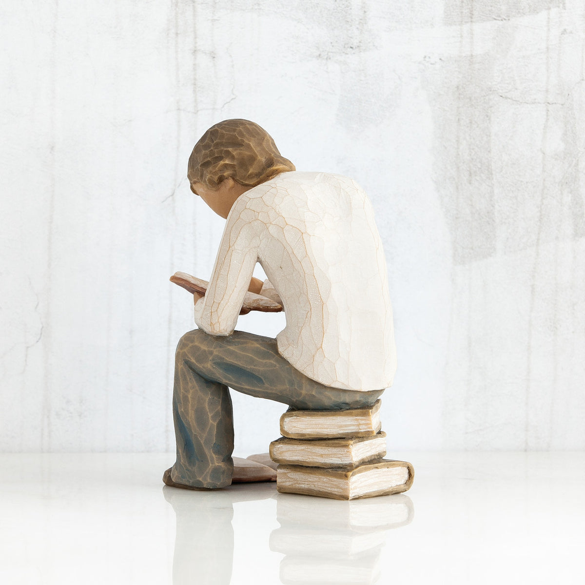 Back view of brunette man figurine in white shirt and blue jeans sitting on books reading a book