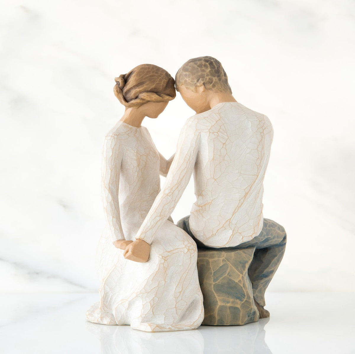 Man and woman figurine in white sitting on rock holding hands facing one another