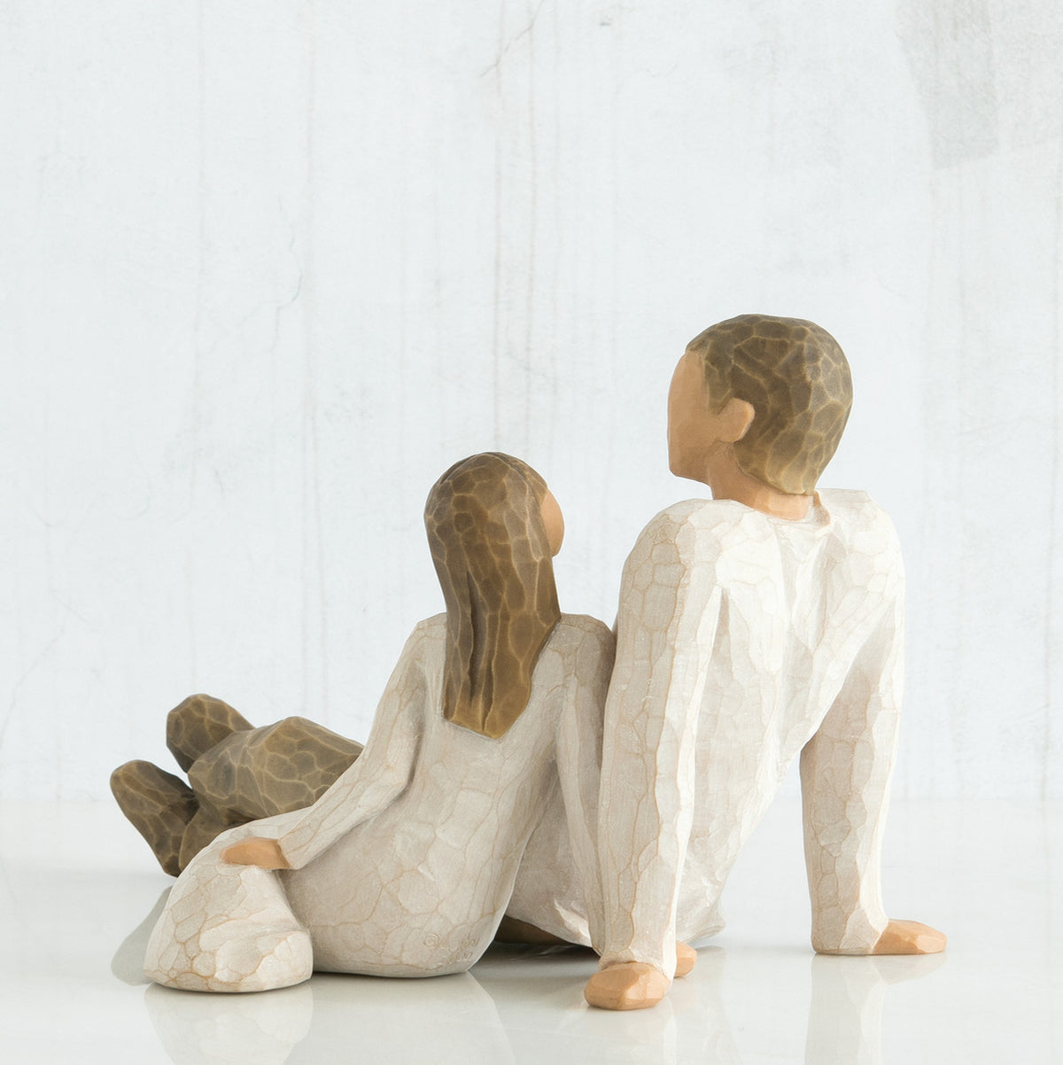 Back view of father figurine sitting next to daughter figurine - both wearing white