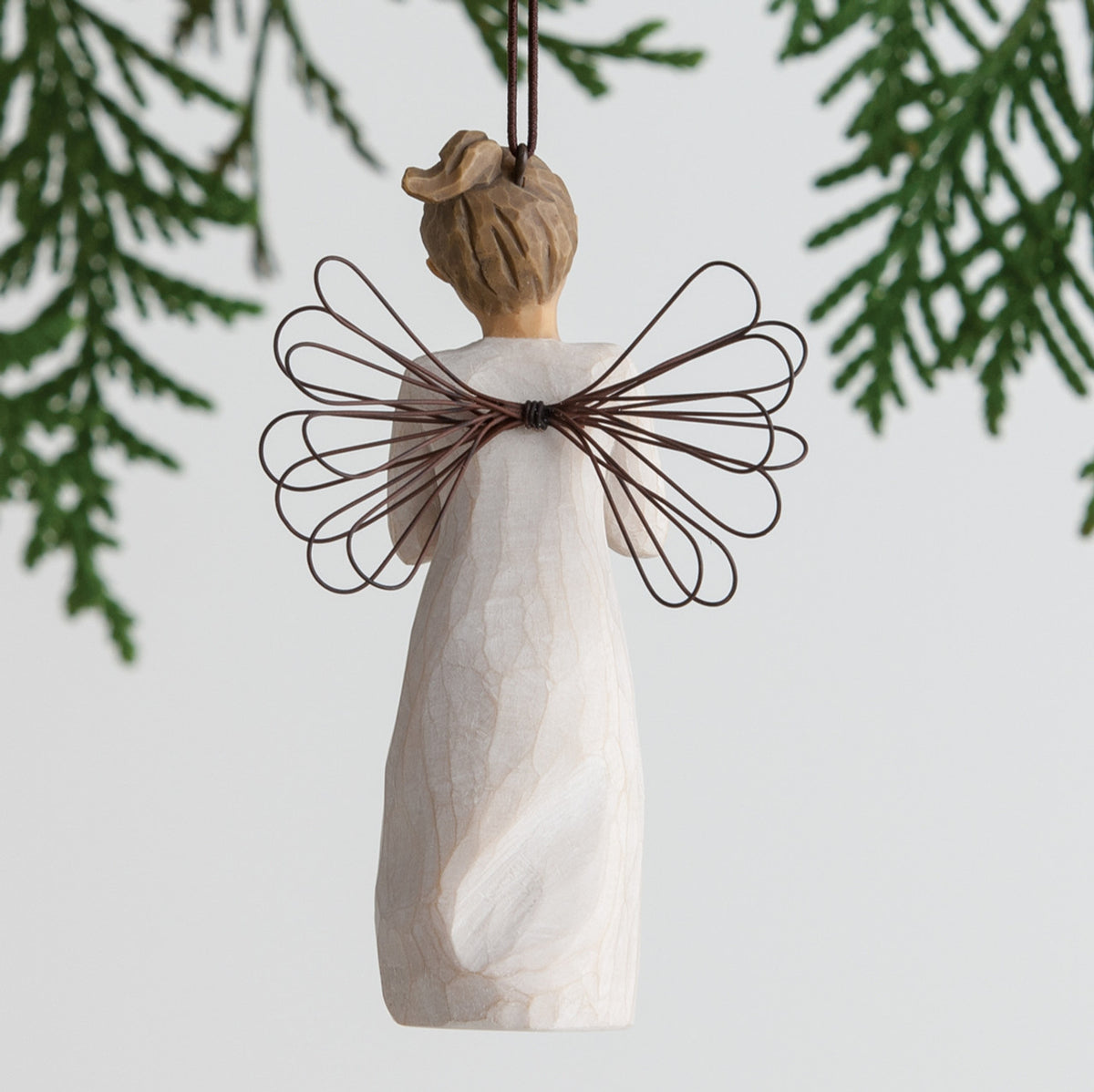 Back view of angel ornament with brown hair in high pony tail leaning forward and holding a red apple up to her face with both hands. Brown string attached to top of angel ornament
