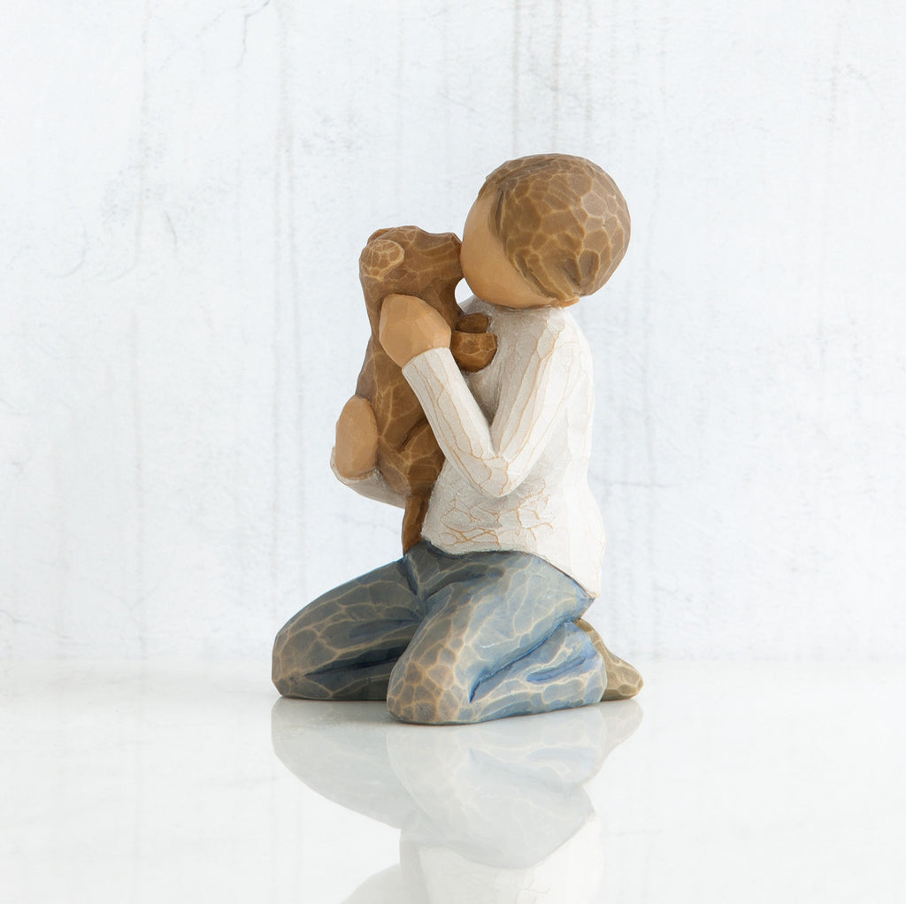 Side view of boy with light brown hair wearing white shirt and jeans and holding a light brown puppy as it licks his face.