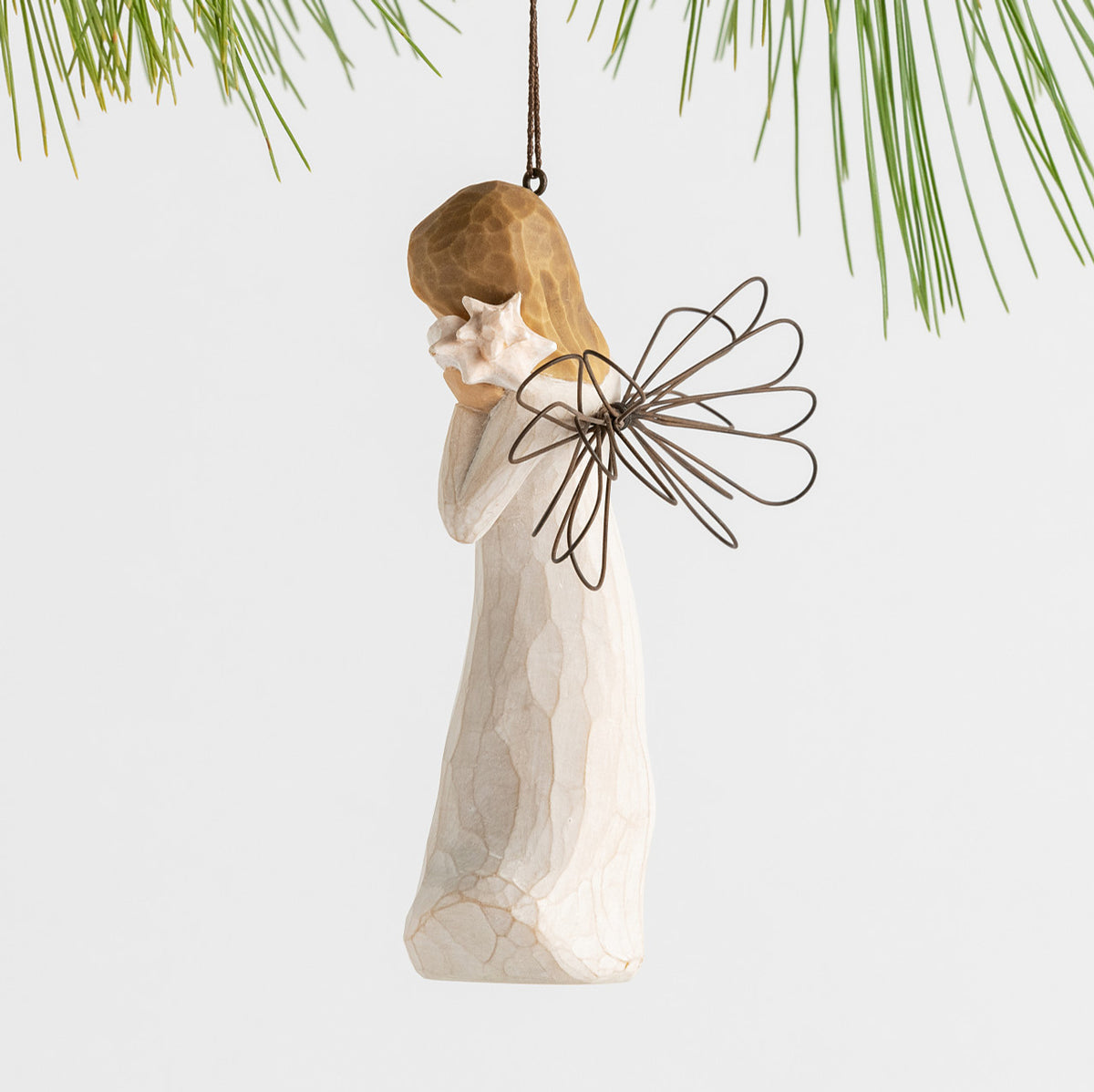 Side view female angel with wire wings in cream dress, holding pink shell up to ear, ornament loop attached to head