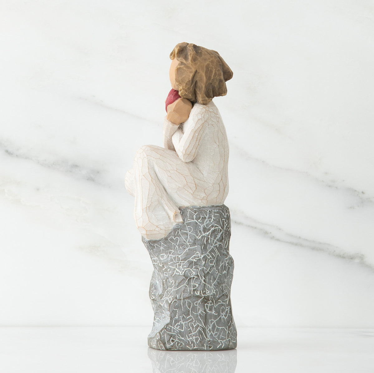 Side view of young girl in white sitting on grey rock with her hands up to her face