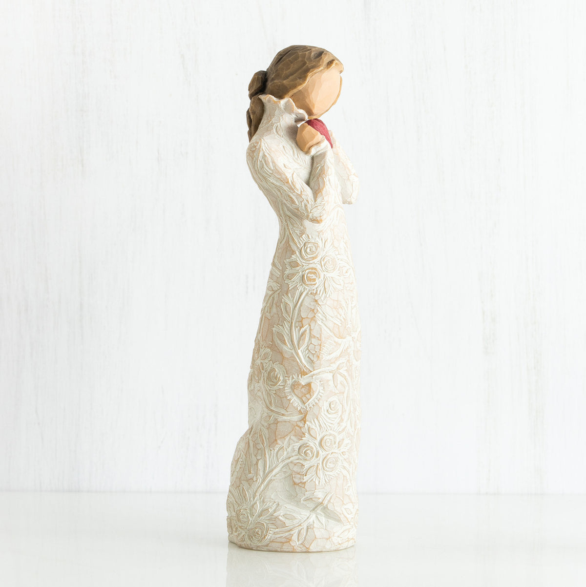 Side view of brunette girl figurine in white dress holding pink hear figurine