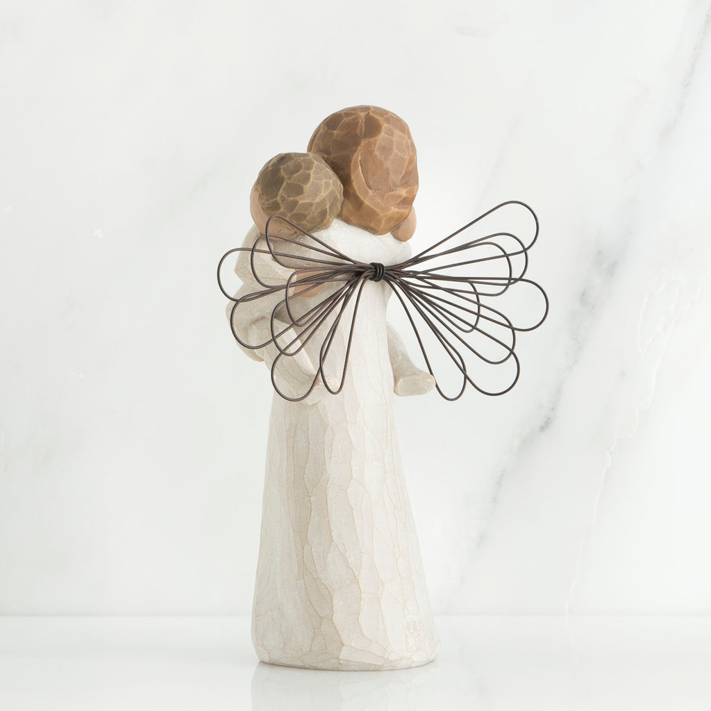 Back view of brunette girl figurine in white dress with brown wings holding baby