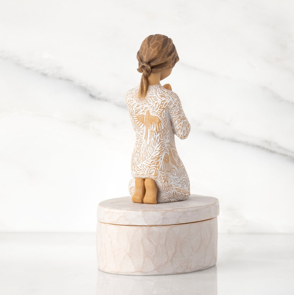 Back view: cream oval resin box, 3-D figure in prayer pose atop lid, in cream dress carved with birds and flowers