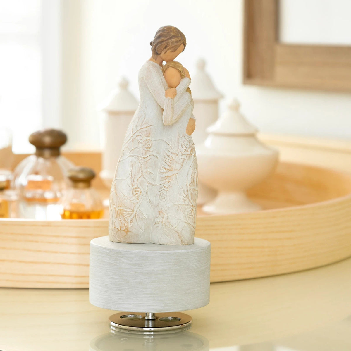 Willow Tree Close to Me Musical, 7.5”h hand-painted resin figure of woman embracing tween girl, both in cream dresses carved with intertwined vines and leaves, atop round, cream base containing musical element, on dressing table