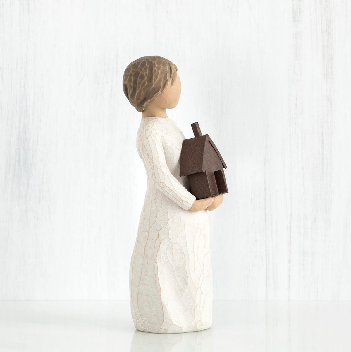 Small brown haired girl figurine in white dress holding brown house figurine