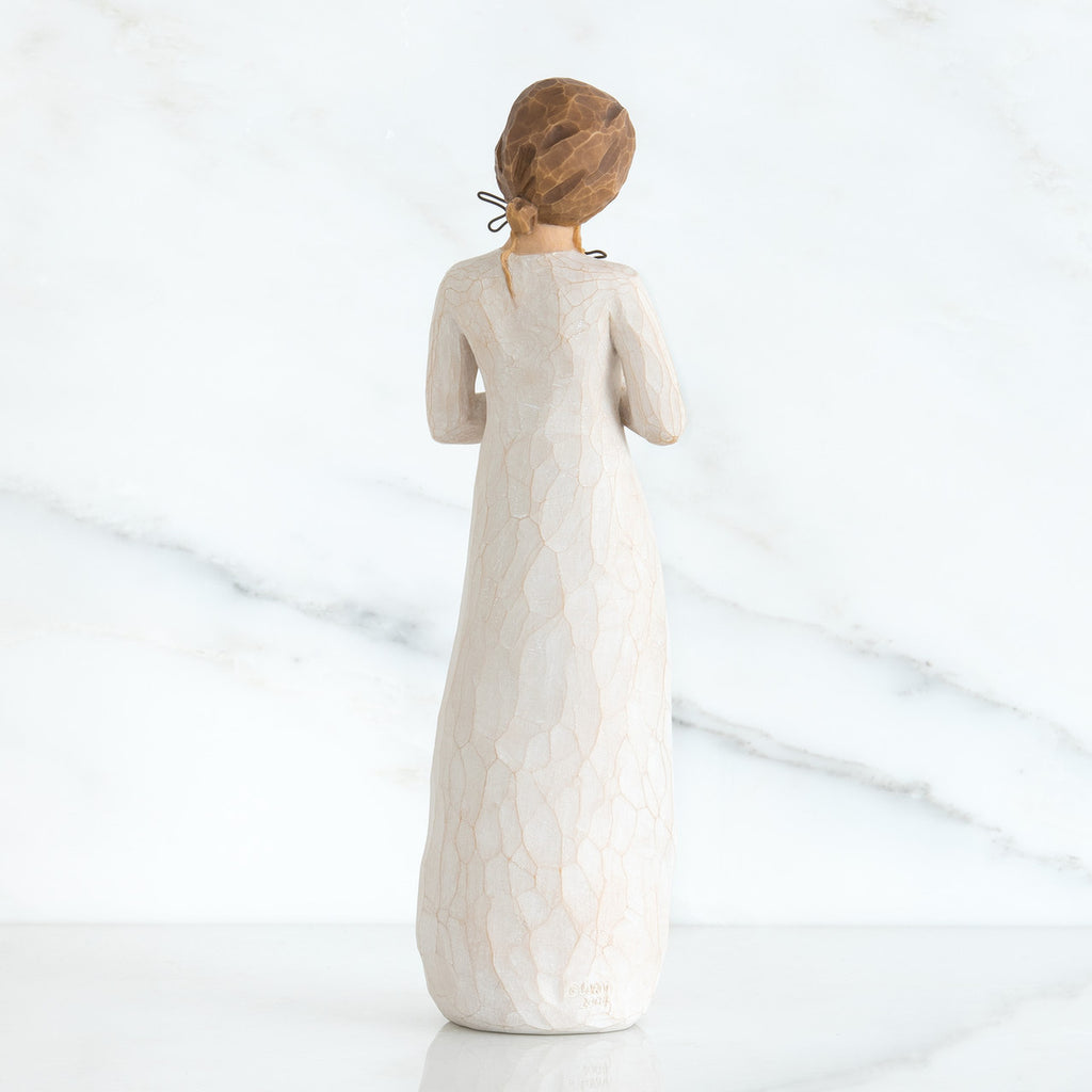 Back view of girl with brown hair in a bun holding three flowers with long stems up to her chest with both hands