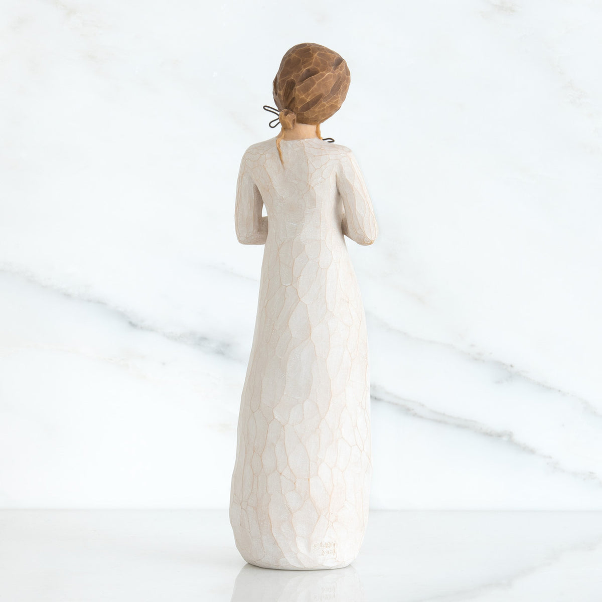 Back view of girl with brown hair in a bun holding three flowers with long stems up to her chest with both hands