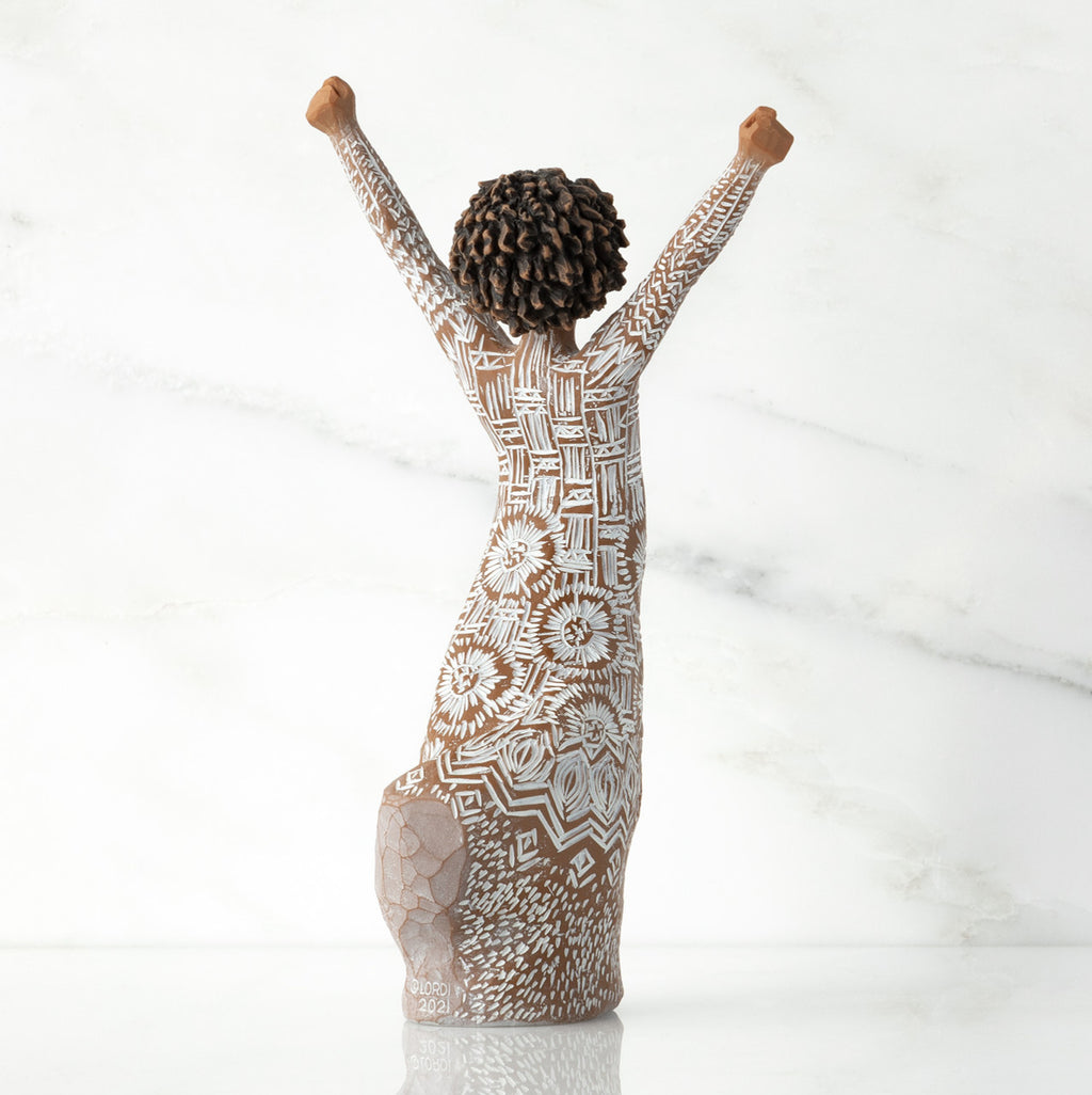 Right back of figure, with arms raised overhead, dress etched with African textile patterns