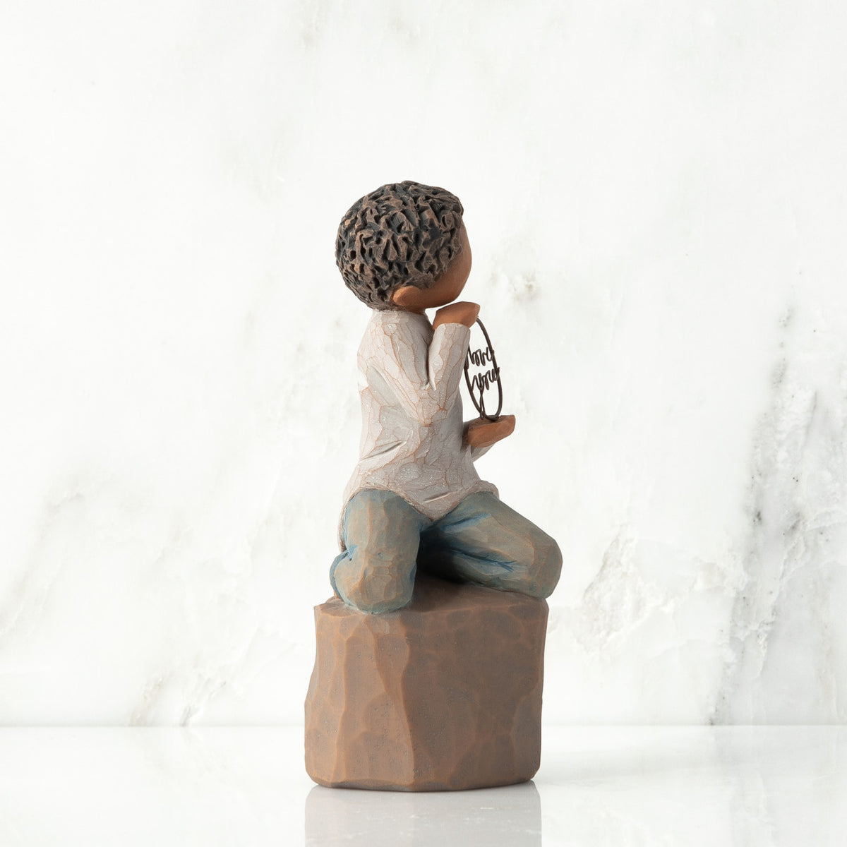 Left view: Figure of darker-skin child, kneeling on rock, holding wire circle with ‘love you’ written in wire
