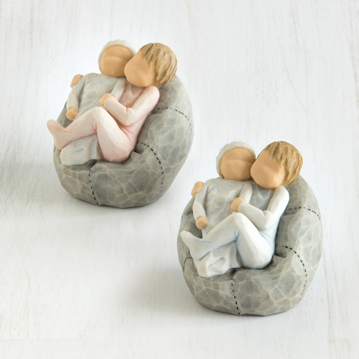 Set of two grey bean bags with two small baby figurines sitting hugging one another on it