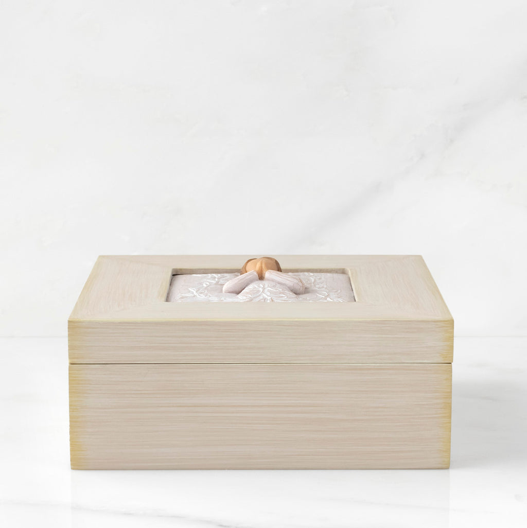 Side View: Cream square wood box with hinged lid, carving on lid of female in cream dress with hands in prayer position, surrounded by leaves and vines