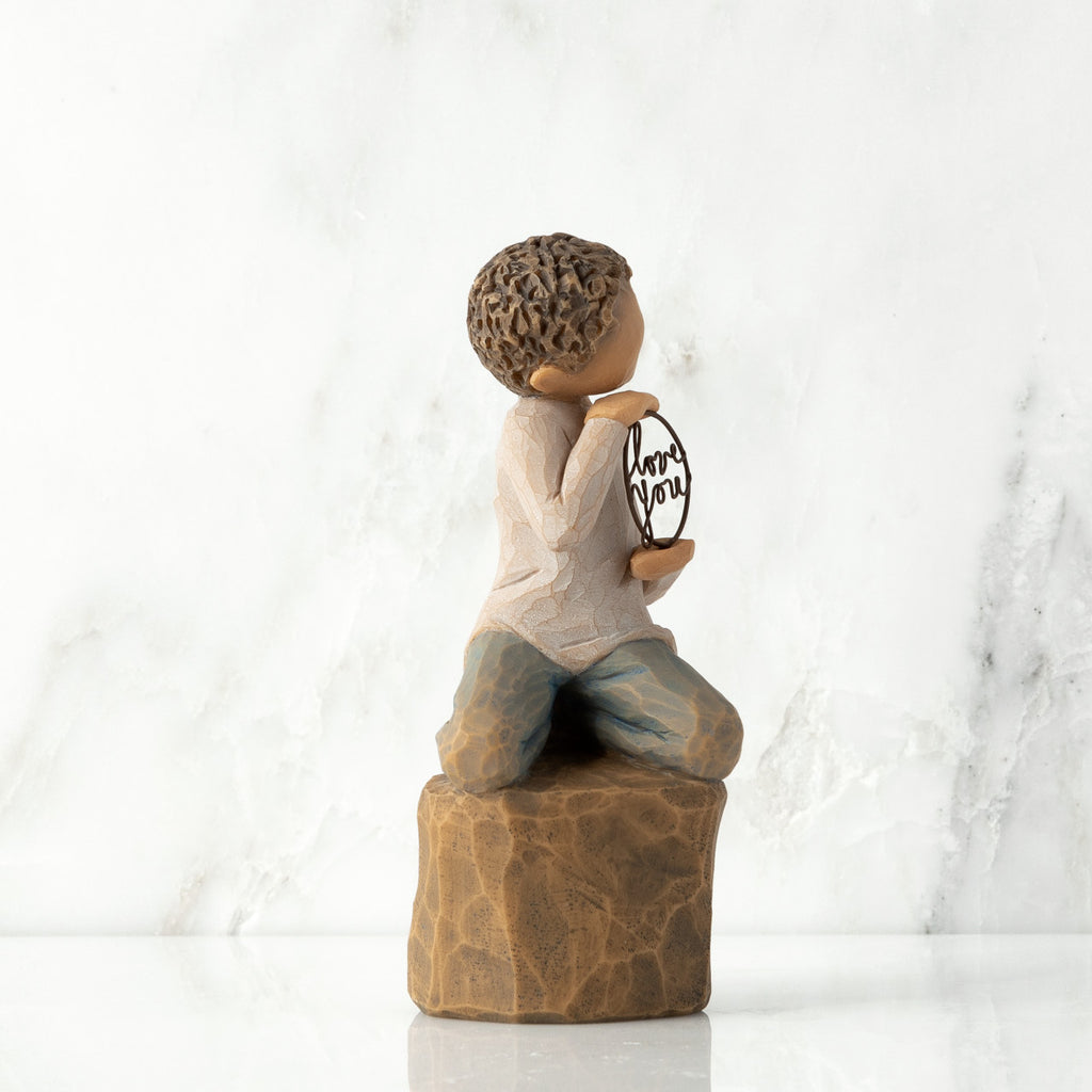 Right view: Figure of lighter-skin child, kneeling on rock, holding wire circle with ‘love you’ written in wire