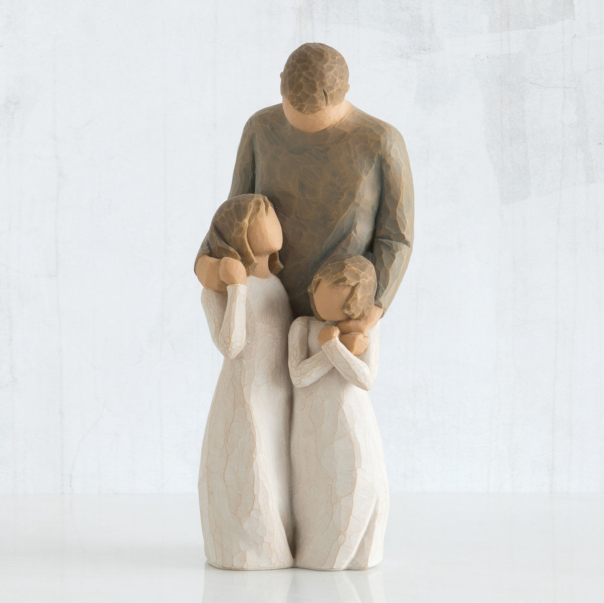 Man faceless figurine wearing brown shirt standing over two faceless girl figurines in white dresses