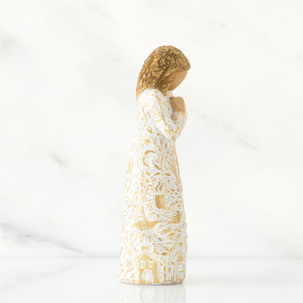 Gold haired girl figurine in white / gold dress facing the side holding her hands to her chest - white background