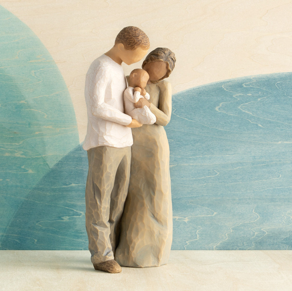 Front view of standing couple, woman has darker skin and hair; man has lighter skin and hair, holding a baby between them. Blue painted background.