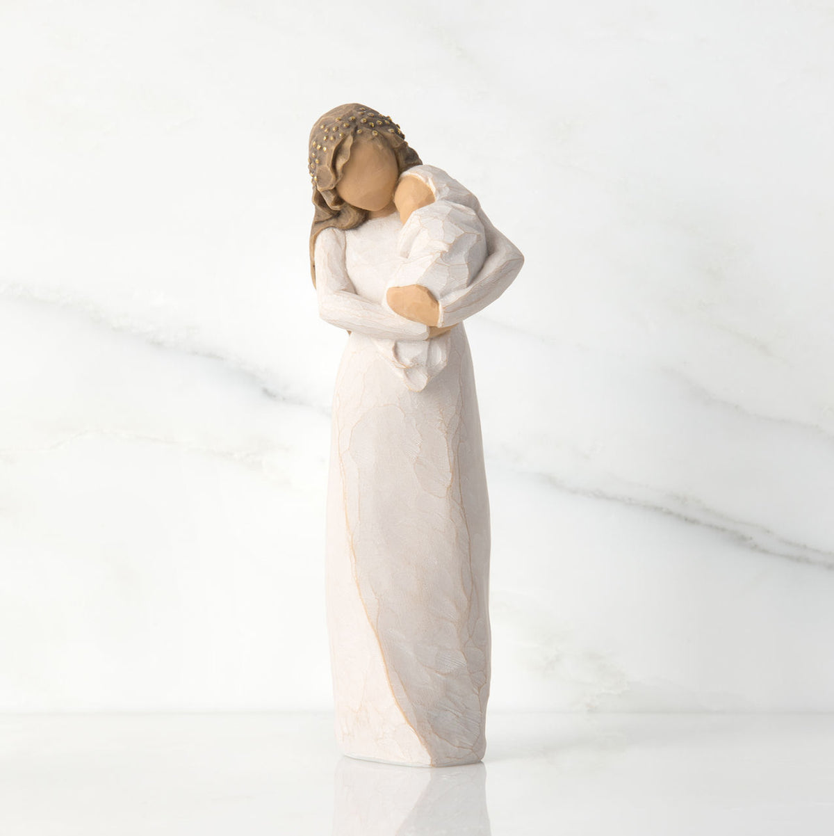 Front view of brunette woman figurine in white dress holding swaddled baby