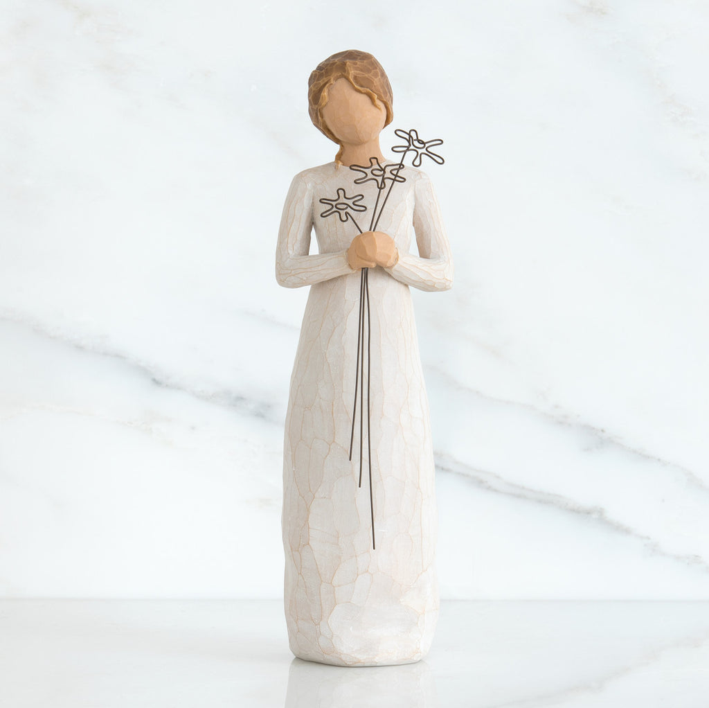 Front view of girl with brown hair in a bun holding three flowers with long stems up to her chest with both hands