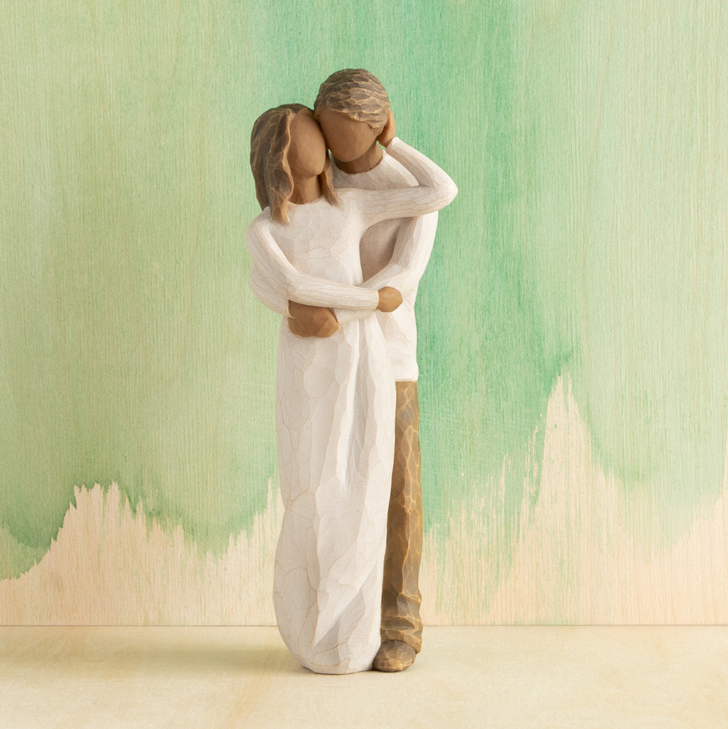 Front view of couple, standing with arms around each other. Woman and man have darker skin tones and hair color. Green painted background.