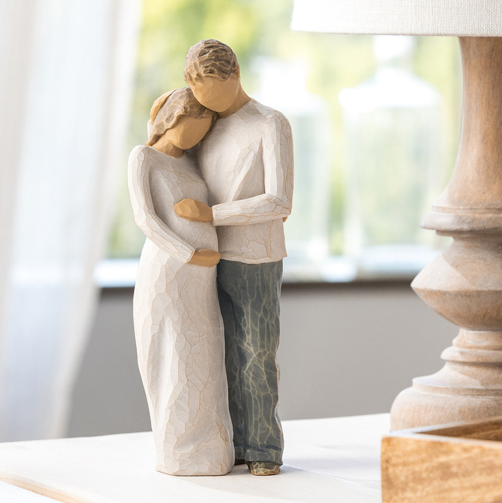 Willow Tree Home, 8.5”h hand-painted standing figure of man and pregnant woman embracing, both in neutral clothes, on table near window