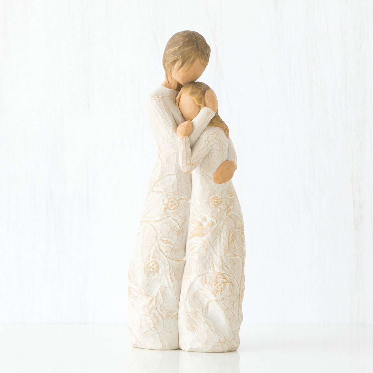 Mother faceless figurine hugging faceless daughter figurine - both standing wearing white dresses