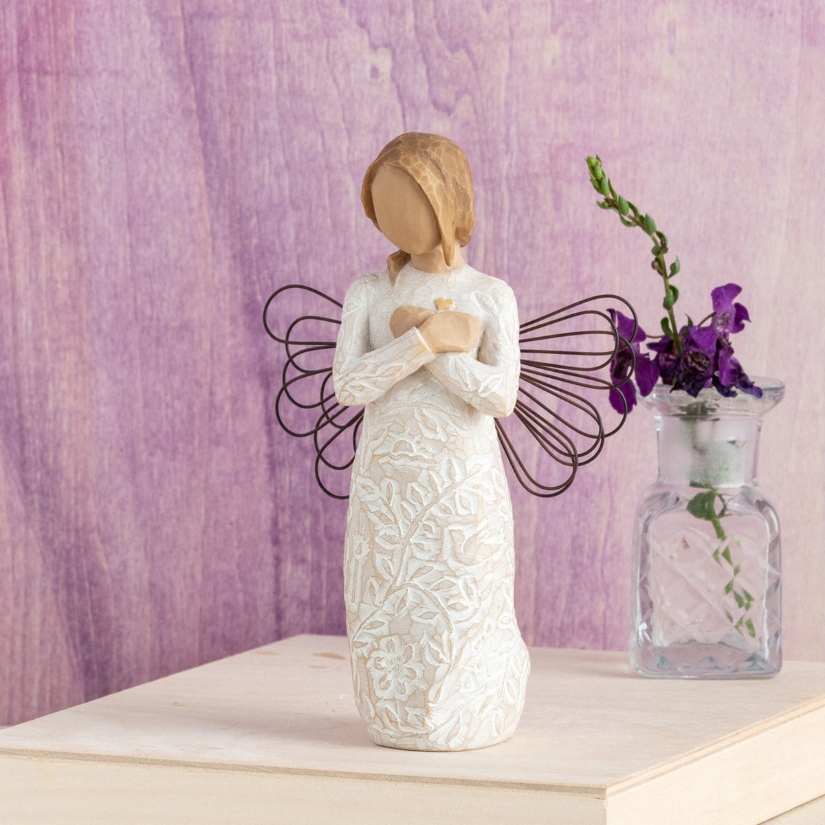 Willow Tree Remembrance, 5”h hand-painted standing resin angel figure in cream dress carved with symbols of nature, wire wings, crossed hands under small gold-leaf heart, in front of purple painting