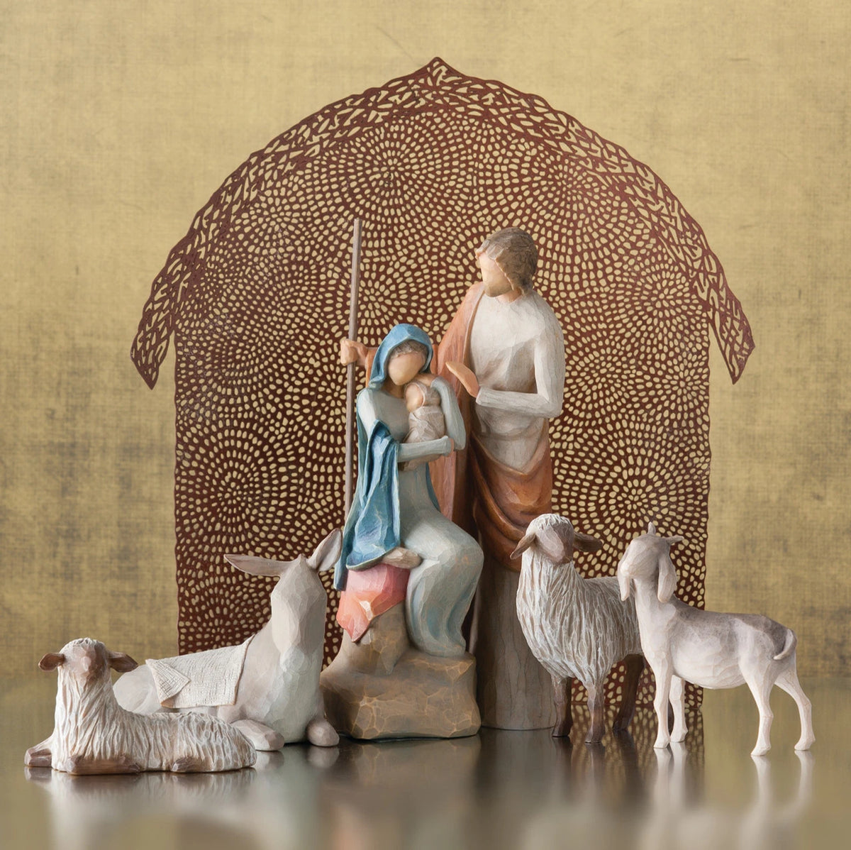 Mary and joesph figurines holding baby with four sheep figurines around them - brown sheer barn paper behind them