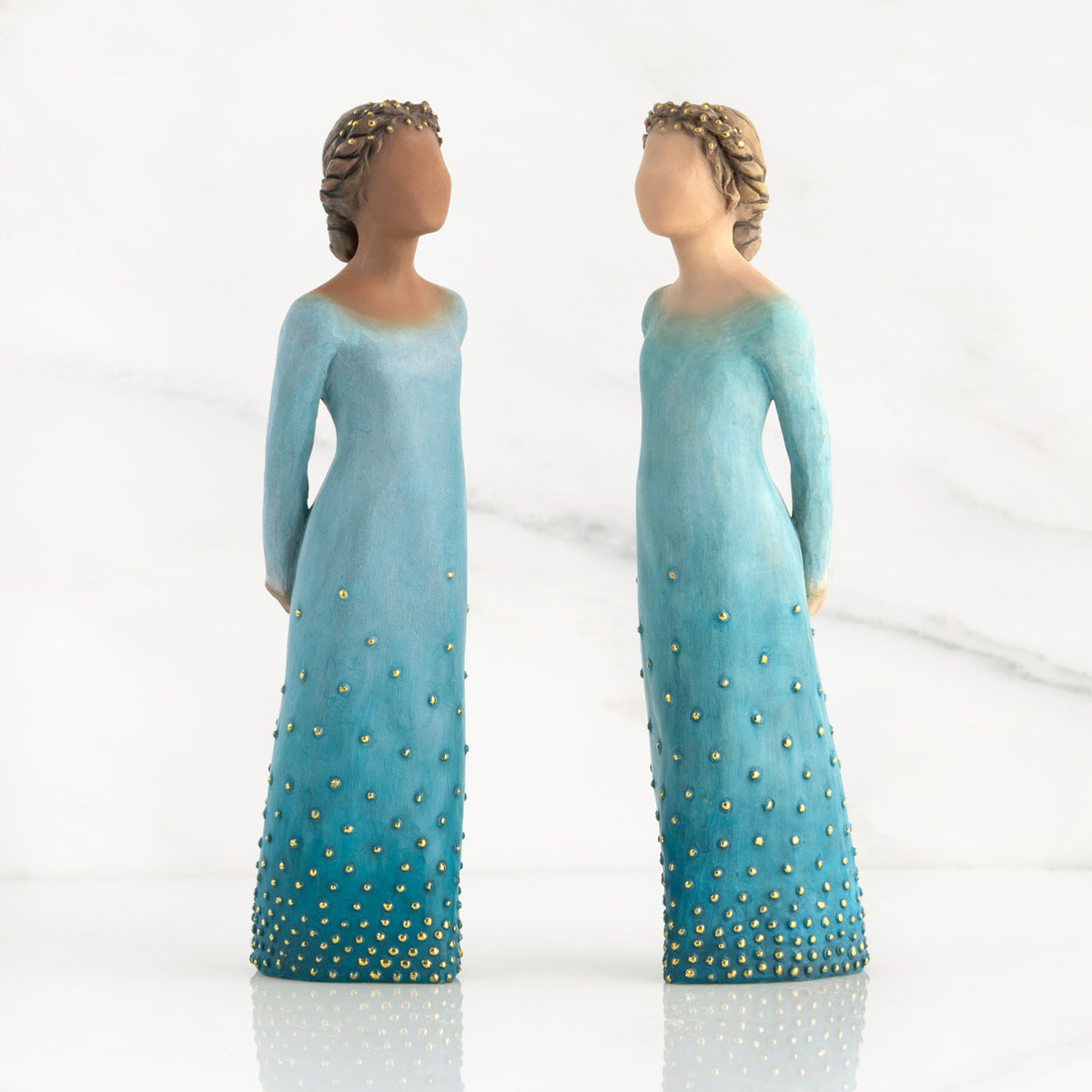 Front view of both lighter and darker-skin figures, arms clasped behind backs, hair and deep blue ombré garments dotted with gold leaf.
